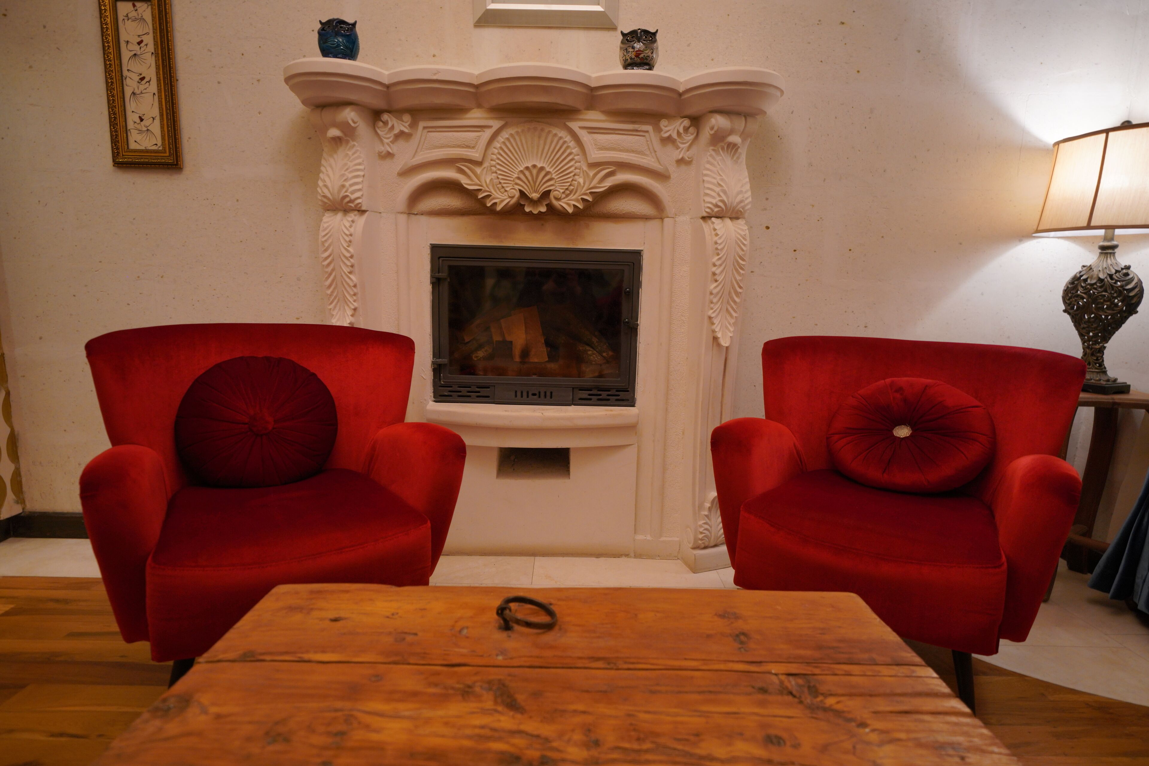 Una habitación con dos sillones rojos, una mesa de centro de madera, una chimenea con repisa y un cuadro enmarcado en la pared.