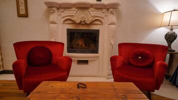 Una habitación con dos sillones rojos, una mesa de centro de madera, una chimenea con repisa y un cuadro enmarcado en la pared.