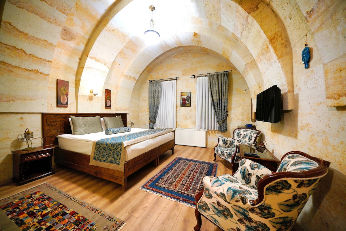 Une chambre à coucher avec un lit en bois, un tapis à motifs, une chaise et un téléviseur fixé au mur.