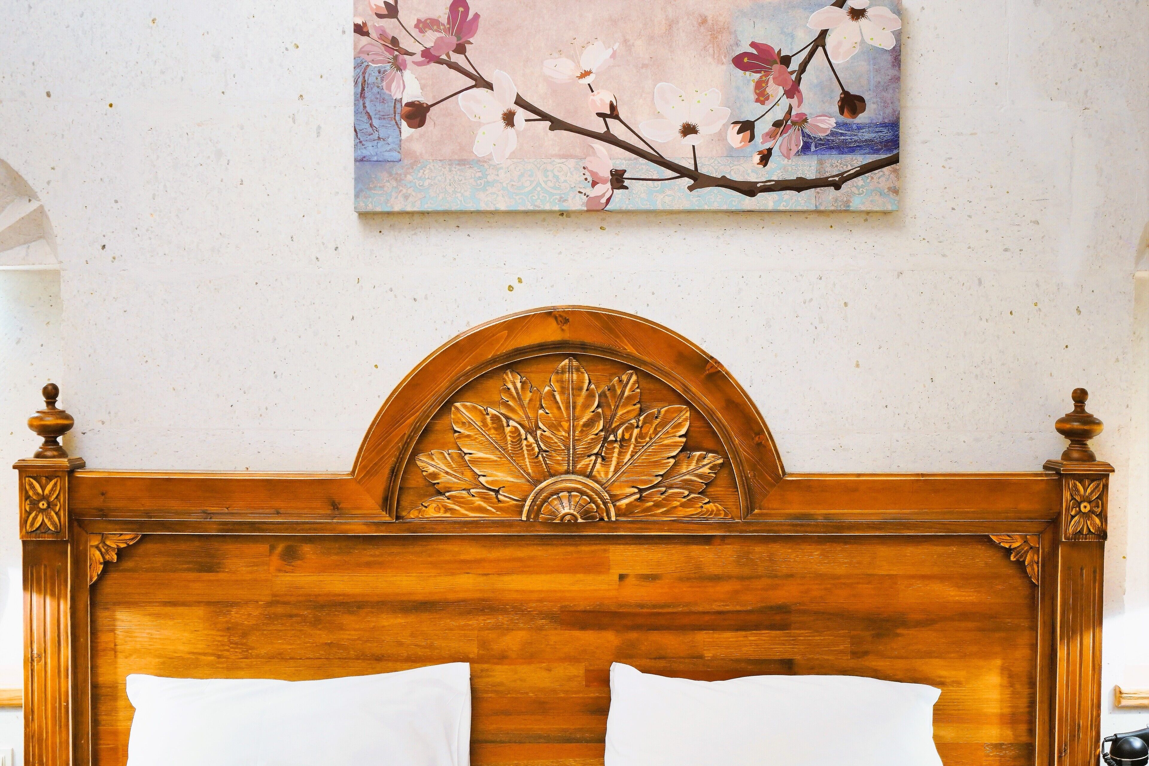 Cabecera de madera con diseño floral, almohada blanca y un cuadro de cerezos en la pared.
