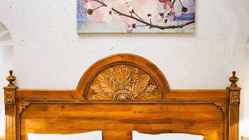 Cabecera de madera con diseño floral, almohada blanca y un cuadro de cerezos en la pared.