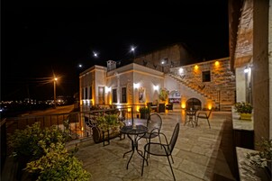 An outdoor patio area with stone flooring, metal chairs, and tables. There is a staircase leading to an upper level.