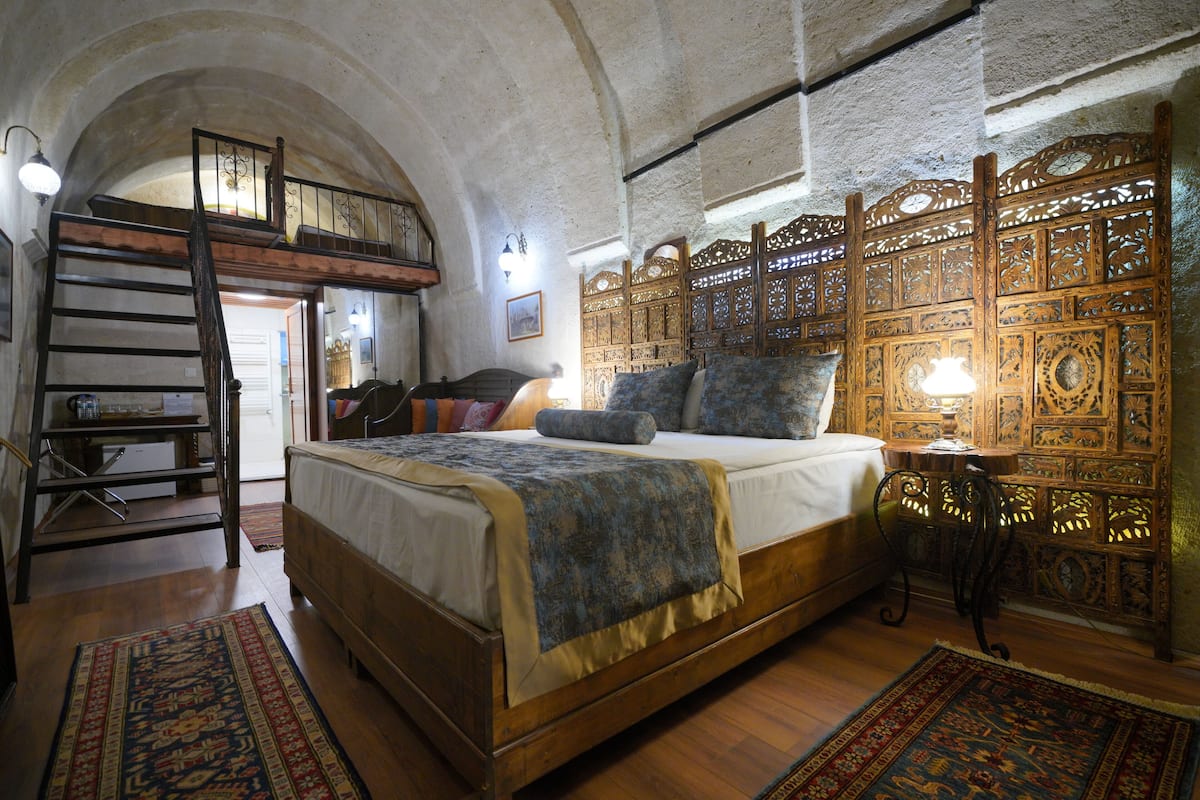 Une chambre avec un lit en bois, un escalier de style industriel et une cloison décorative en bois.
