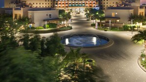 Un hotel con un patio central, palmeras y una fuente.
