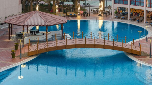 Una piscina con un puente de madera, sillas de descanso y mesas.