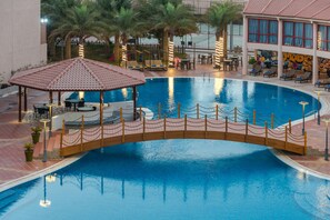 A pool with a wooden bridge, lounge chairs, and tables. - Al Reem Village Hotel (Al Jubail)