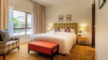 Habitación de hotel con una cama grande, una silla, una mesita y un ventanal con cortinas.