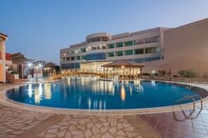 A swimming pool with a bridge, a covered seating area, and a building with multiple balconies. - Al Reem Village Hotel (Al Jubail)