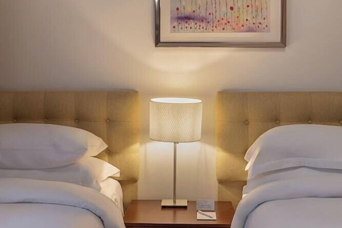 Ett hotellrum med två sängar, ett nattduksbord med en lampa och ett inramat konstverk på väggen.