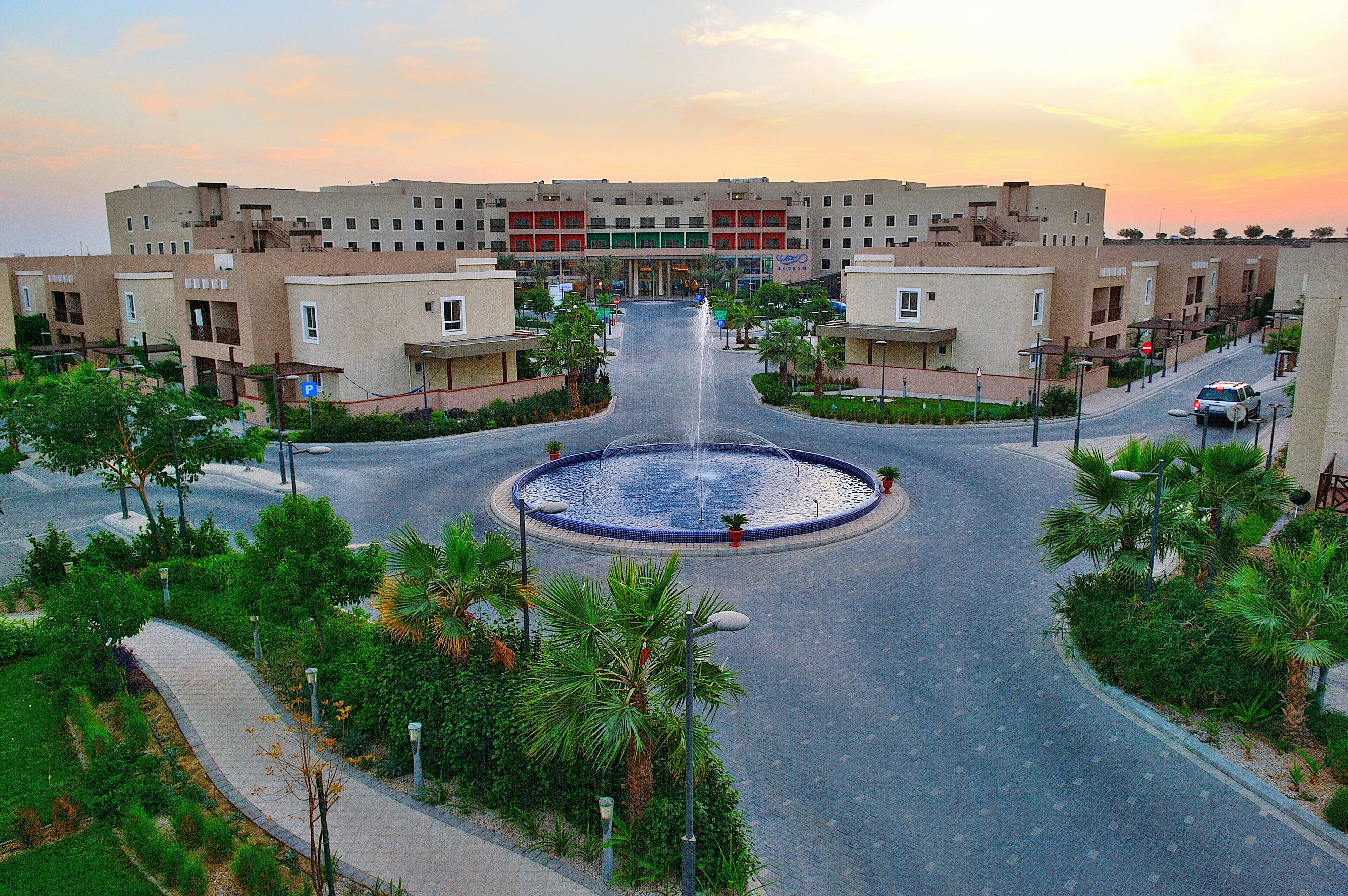A modern hotel with a central fountain, surrounded by palm trees and a landscaped area.