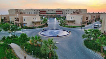 A modern hotel with a central fountain, surrounded by palm trees and a landscaped area.