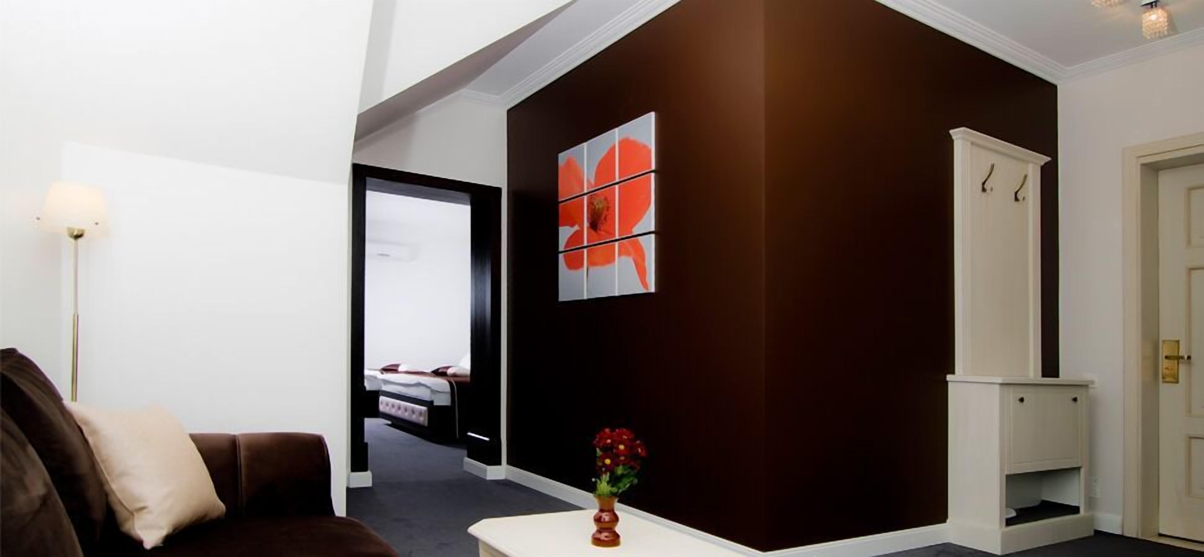A hotel room with a dark brown accent wall, a white door, a bed with a white headboard, and a small white cabinet.