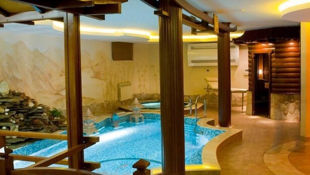 Een wellnessruimte met een whirlpool, houten zuilen en een achtergrond van een stenen muur.
