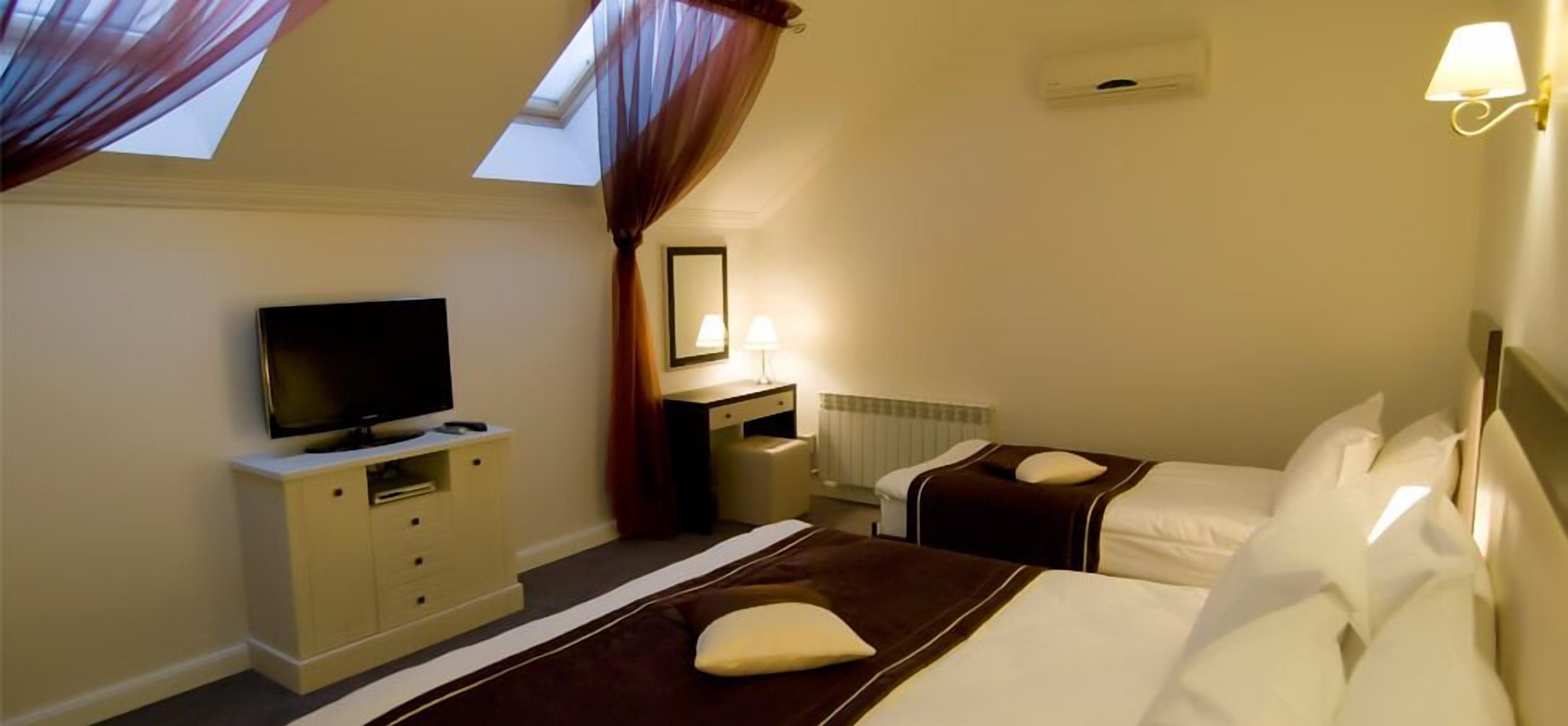 Ein Hotelzimmer mit zwei Betten, einem Fernseher, einem Schreibtisch und einem Spiegel.