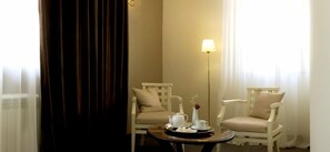 A room with two white chairs, a small round table with a tray of tea set, a floor lamp, and a window with sheer curtains. - Villa Rossa (Chisinau)