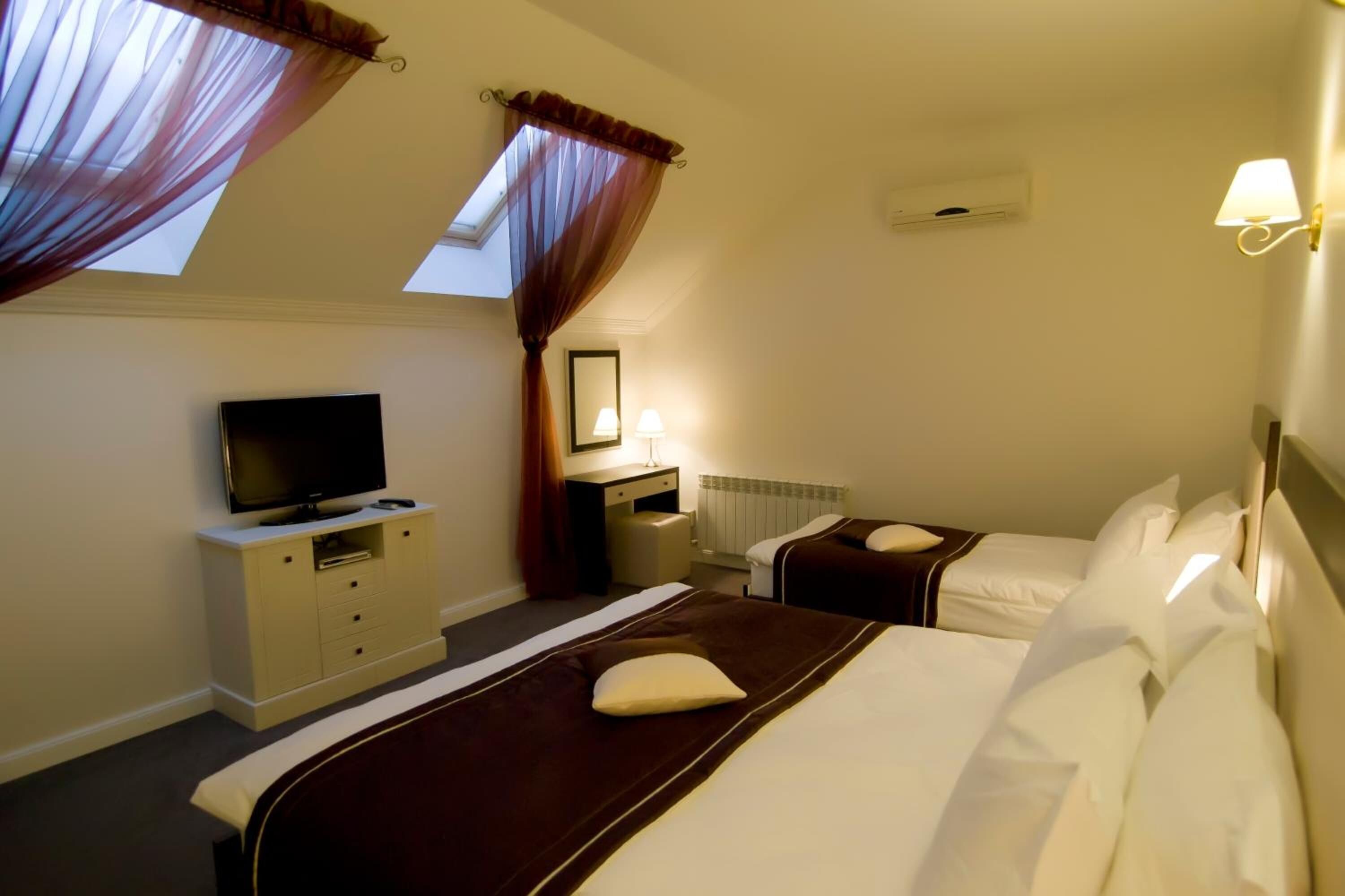 A hotel room with a bed, a TV, a desk, and a window with curtains.