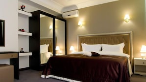 Een hotelkamer met een groot bed, nachtkastjes met lampen, een bureau met stoel, een spiegel en een airconditioning.