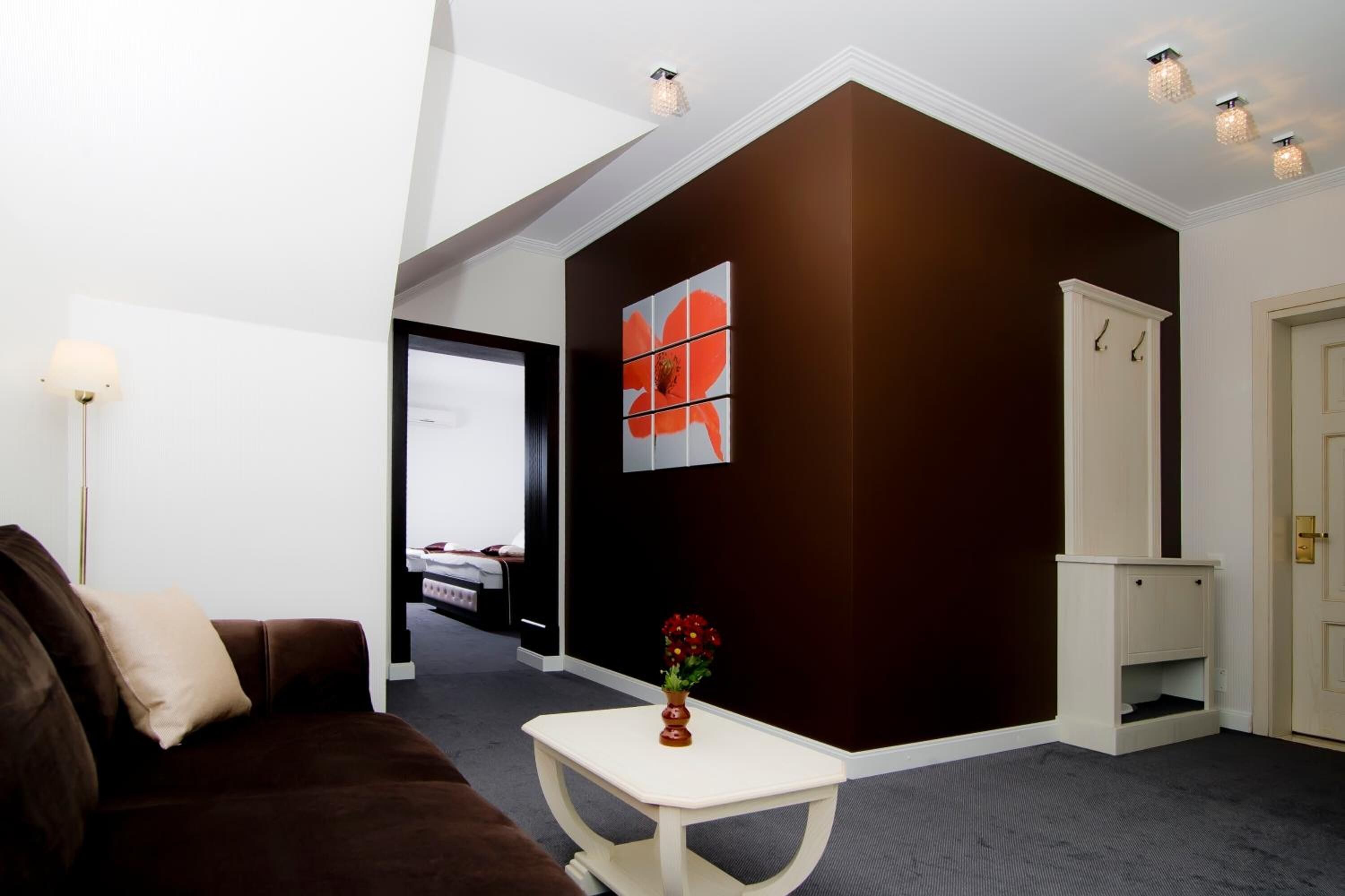 Habitación de hotel moderna con una pared de acento marrón, una mesa blanca con un florero y vistas al pasillo.