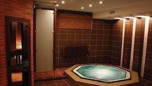Een wellnessruimte met een jacuzzi, betegelde wanden en een houten deur.