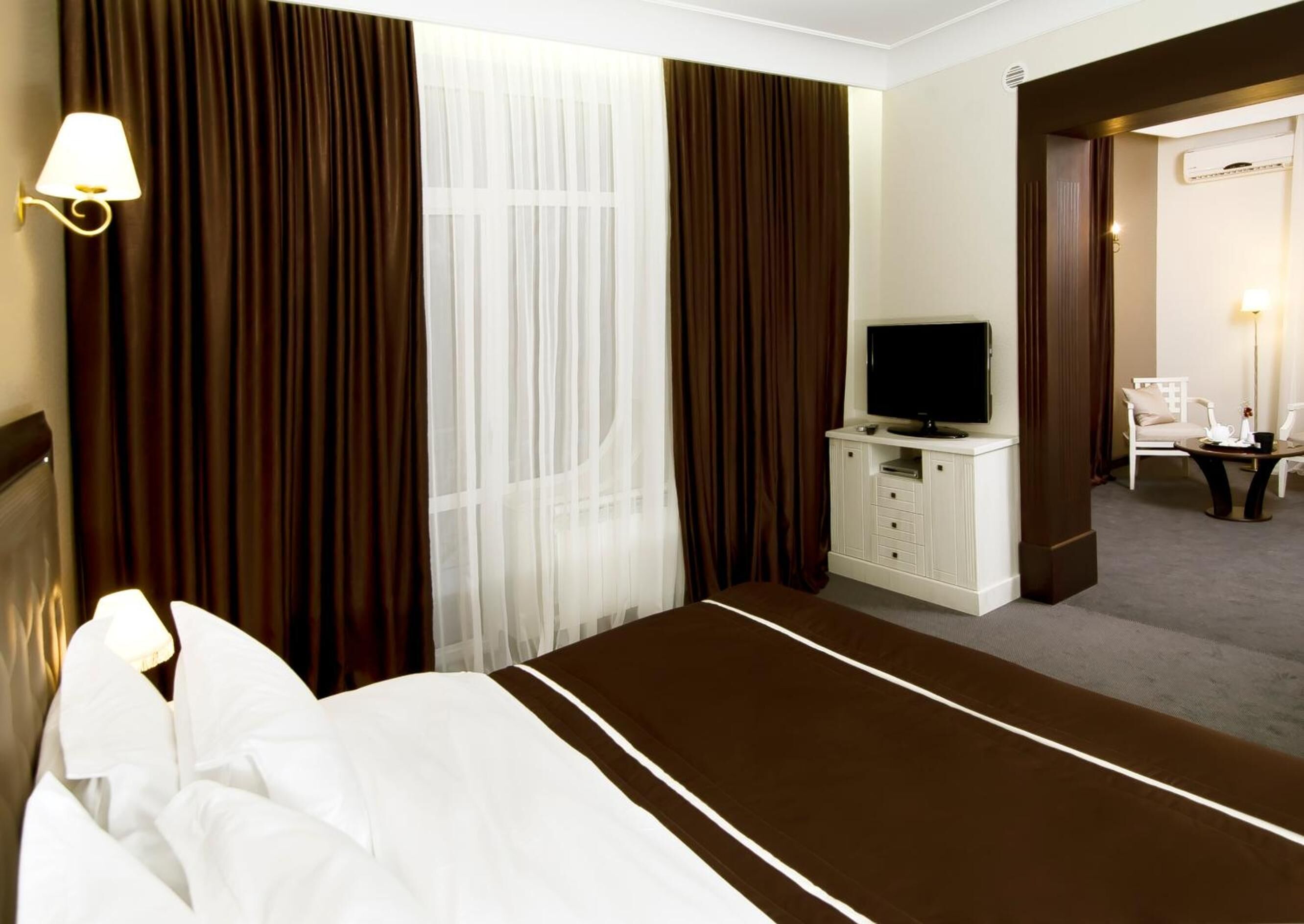 A hotel room with a bed, a TV on a cabinet, a desk, and a chair.