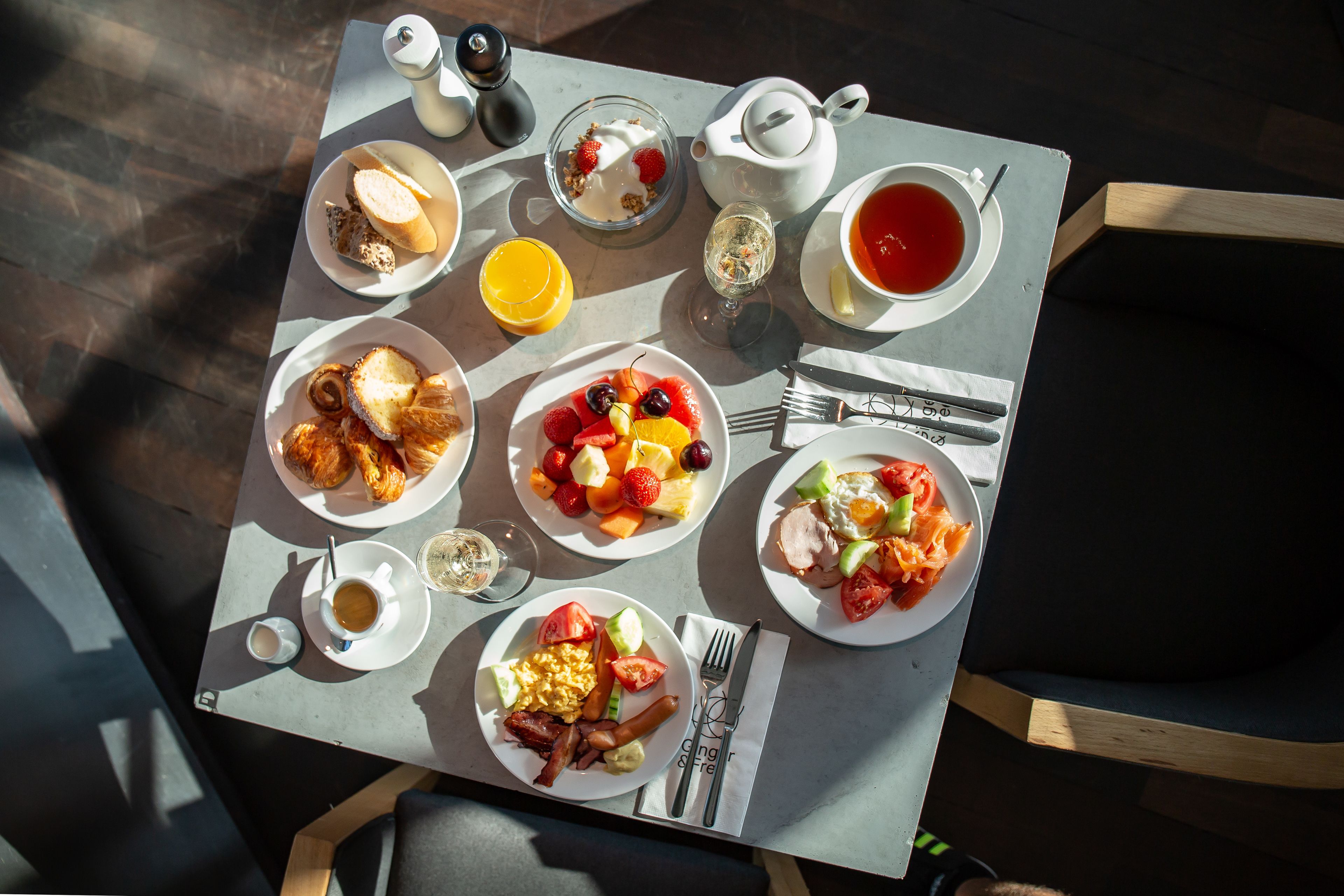 Une table de petit-déjeuner avec divers plats, notamment des toasts, des fruits, des œufs et une tasse de thé.
