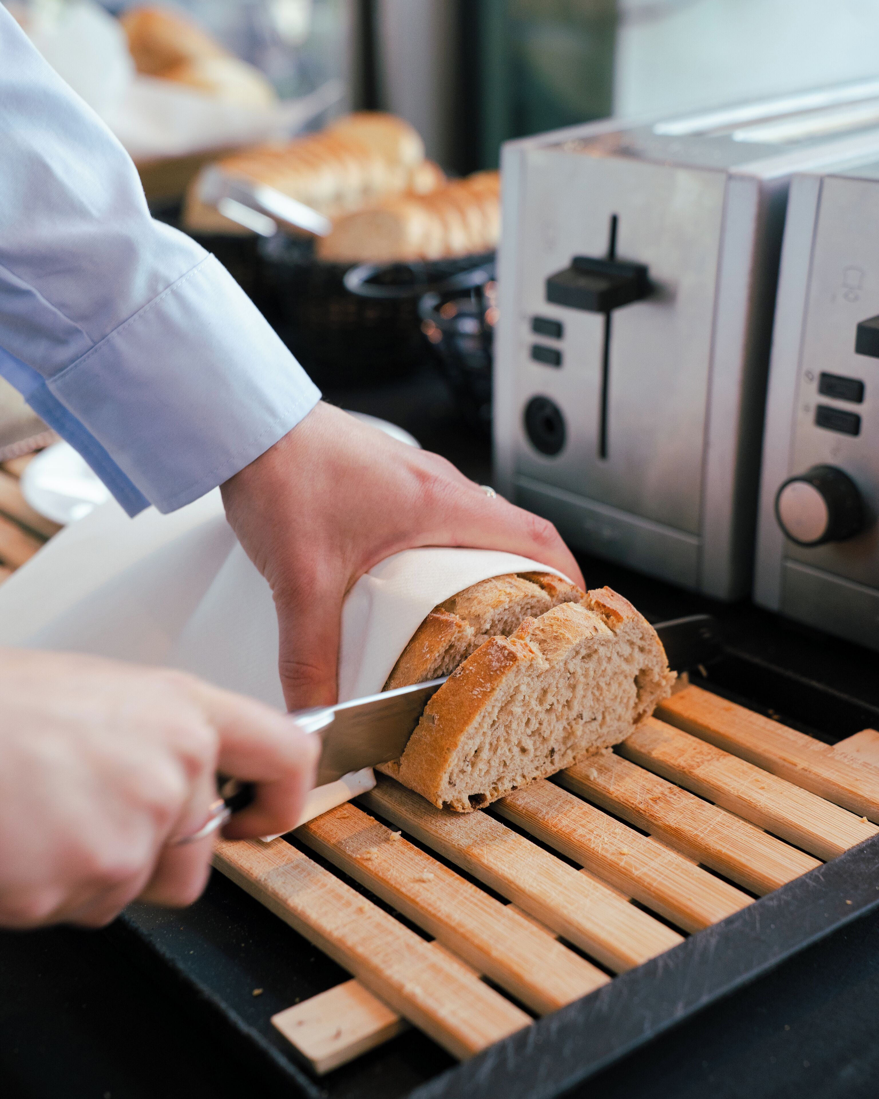 A person slicing bread on a wooden cutting board.