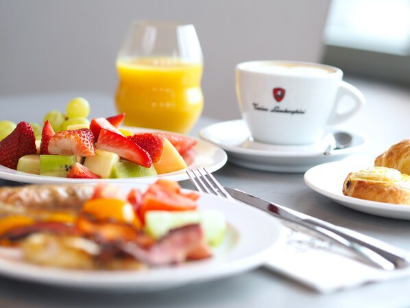 Een ontbijttafel met fruit, een glas sinaasappelsap, een kop koffie en croissants.