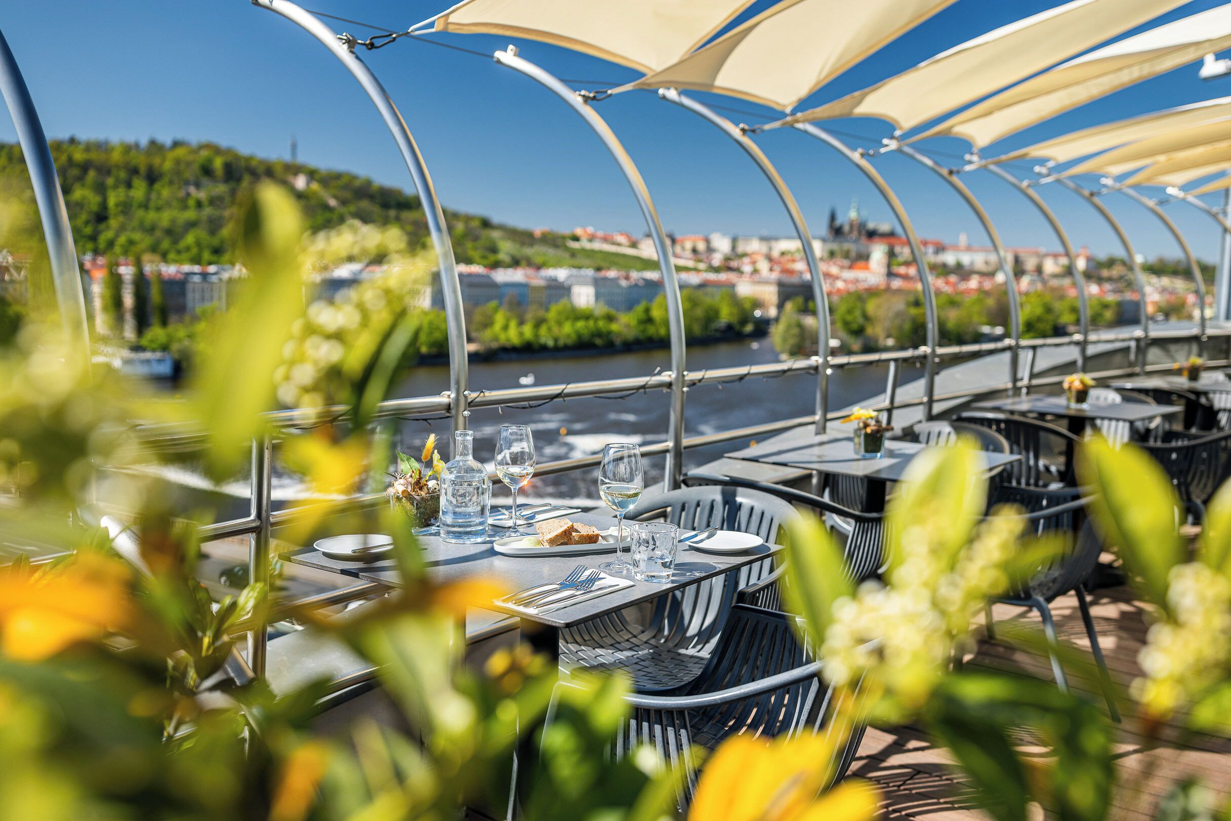 Ein Außenbereich zum Essen mit Tischen und Stühlen, Blick auf einen Fluss und einem überdachten Gang.