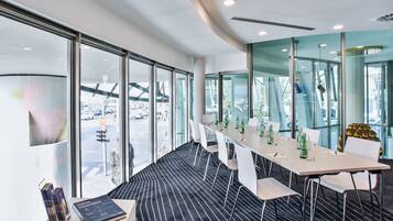 A modern conference room with a long table, white chairs, and glass walls offering a city view.