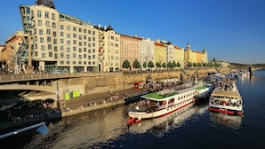 A riverside view with historic buildings, a bridge, and boats. - Dancing House hotel - Tančící dům (Prague)