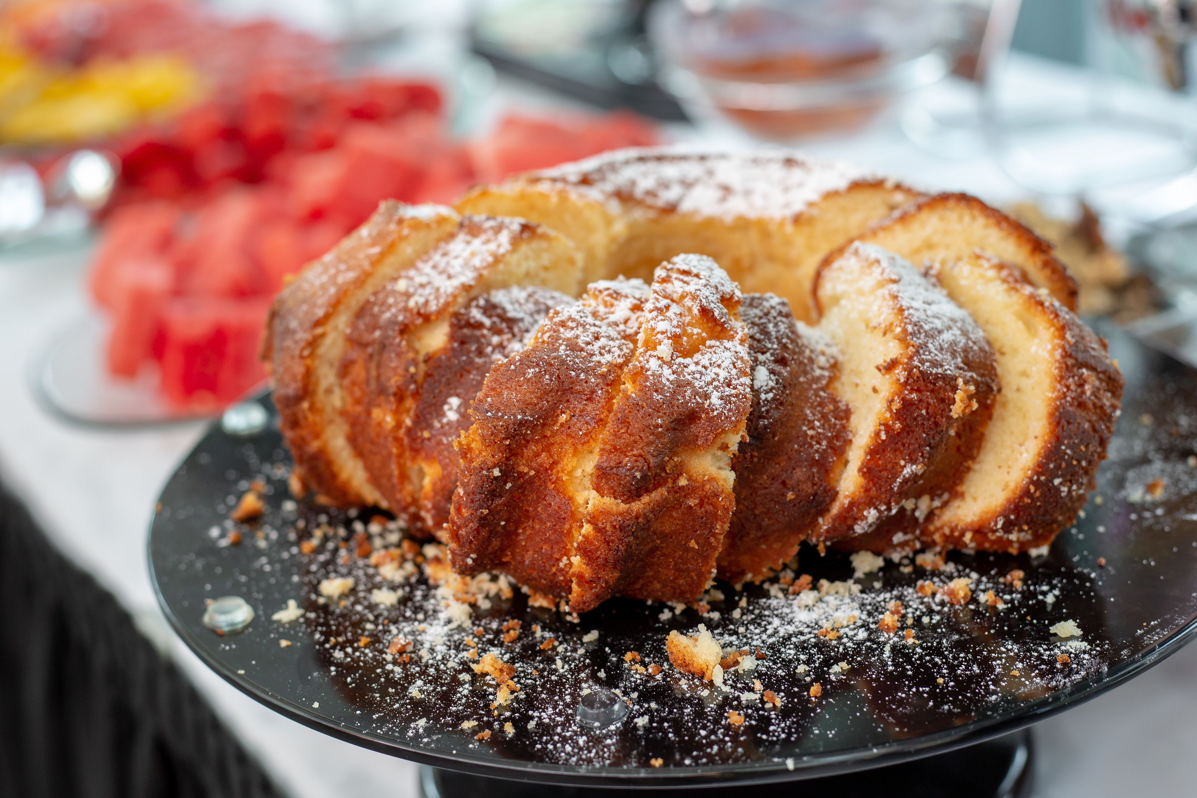 Ein Bundtkuchen auf einem schwarzen Teller mit Krümeln und Puderzucker.