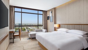 Una habitación de hotel con una cama grande, un escritorio, una silla, una mesita y un televisor.