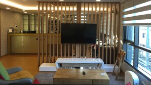 Una sala de estar moderna con televisión, listones de madera, un sofá, una mesa de centro y vistas de la ciudad a través de amplios ventanales.