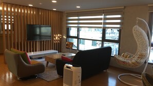 Una sala de estar moderna con un televisor de pantalla plana, asientos cómodos, un ventanal con persianas y una silla colgante.