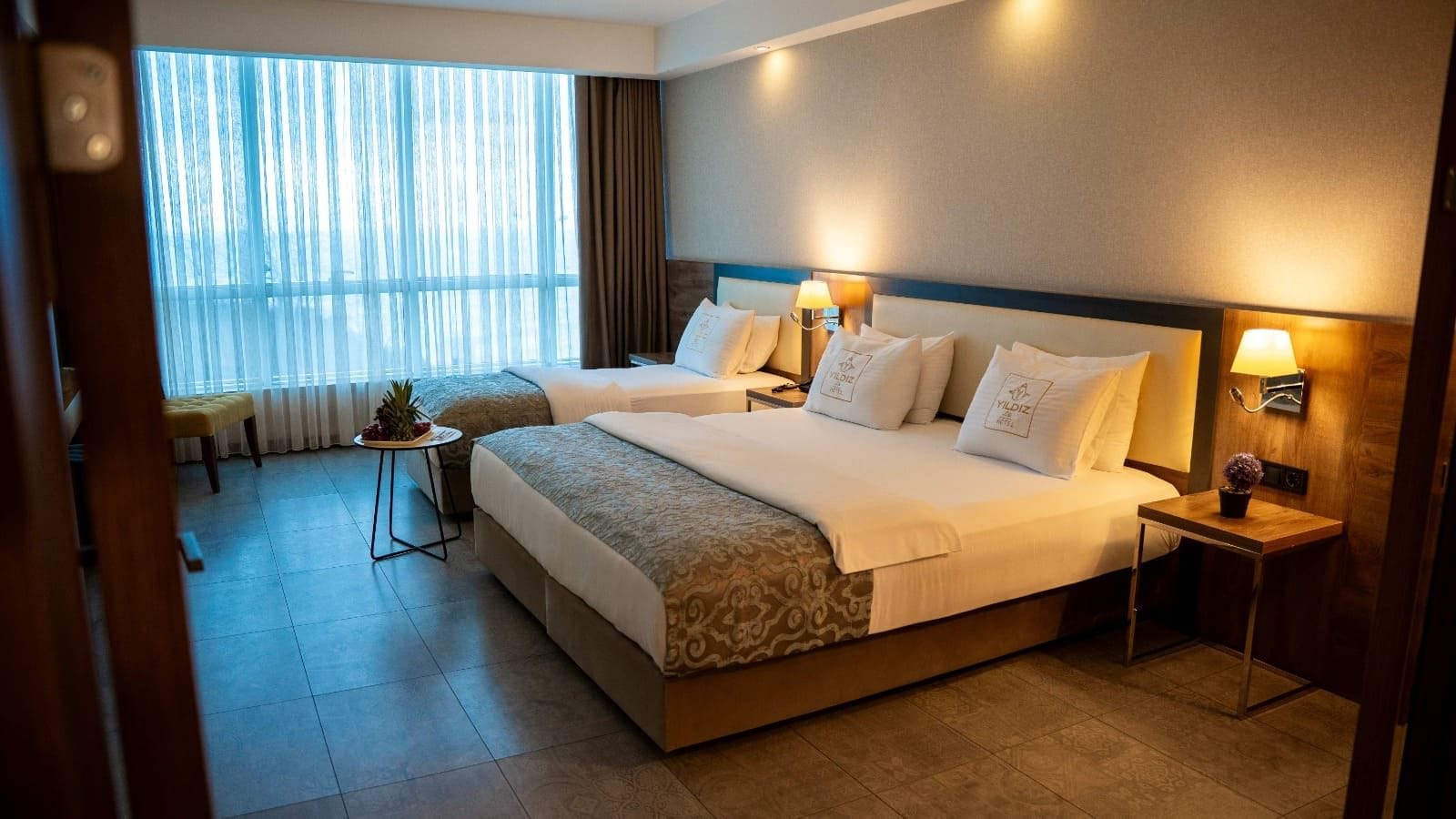 Habitación de hotel con dos camas, una mesita con una planta y una ventana con cortinas.