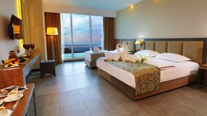 Habitación de hotel con una cama grande, un escritorio con una computadora portátil, una silla y vistas de la ciudad a través de amplios ventanales.