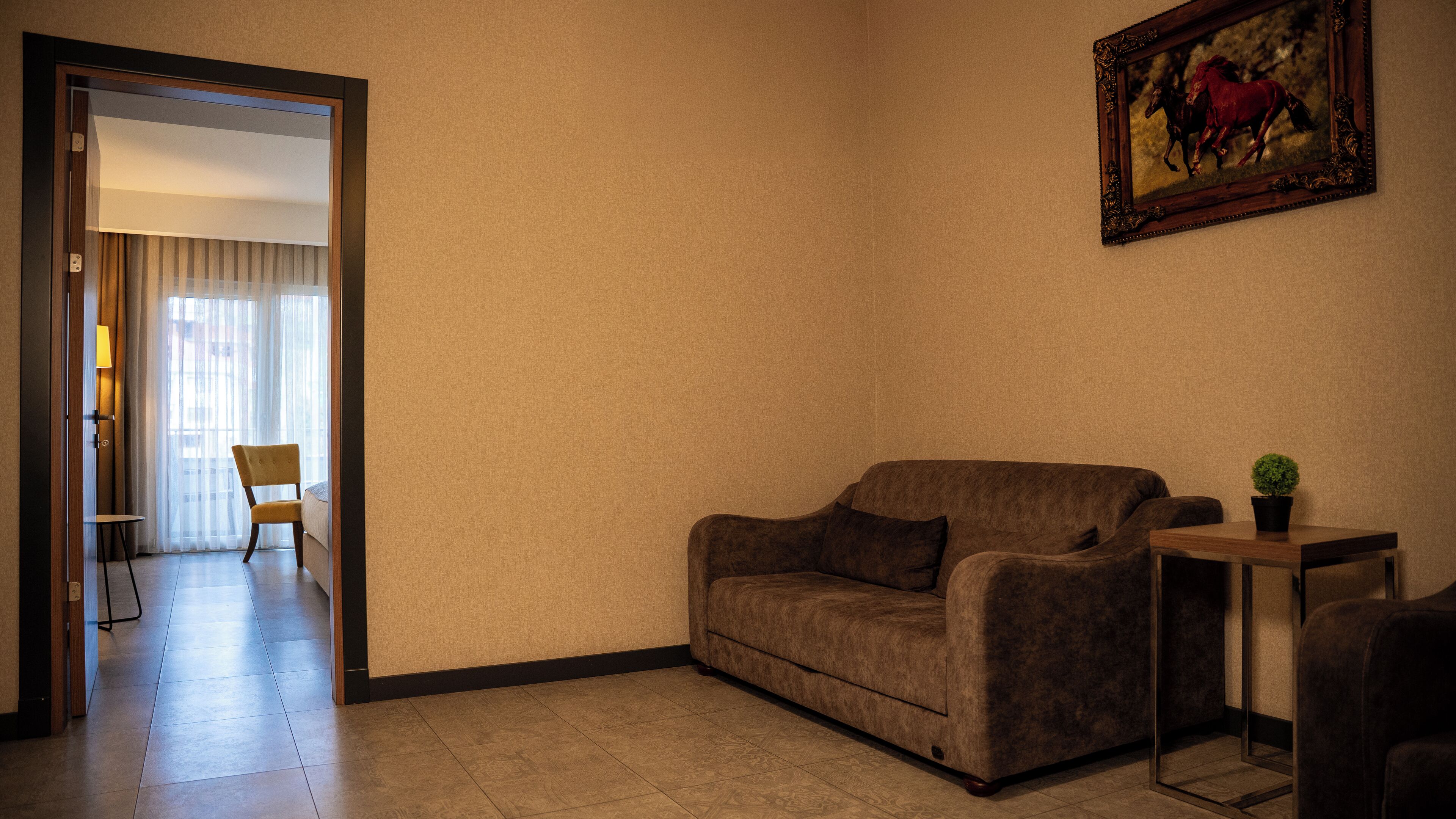A living room with a sofa, a small table, a potted plant, and a painting on the wall.