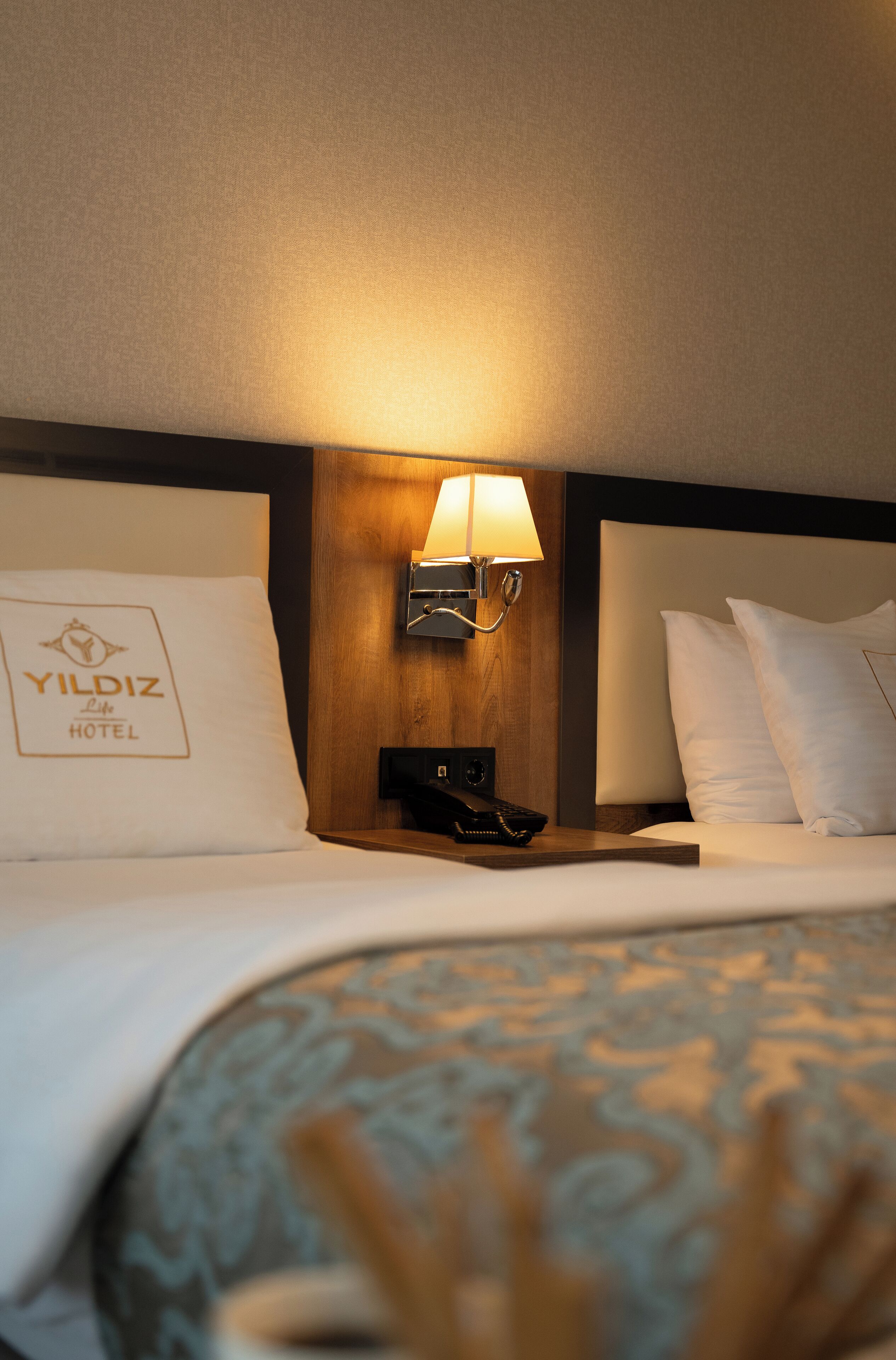 A hotel room with a bed, a nightstand with a lamp, and a pillow with the hotel's name.
