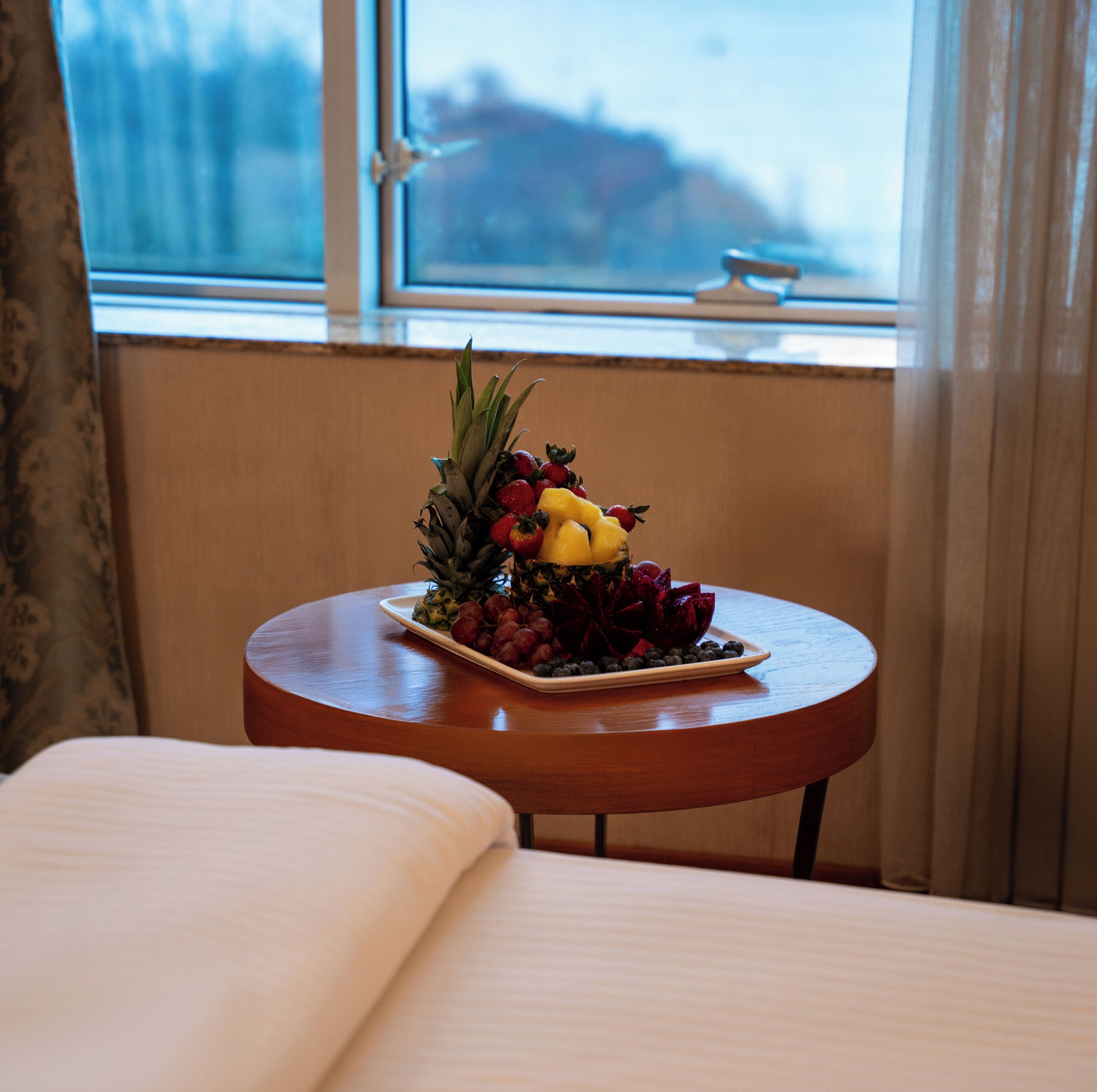 A neatly made bed with a small table beside it, holding a fruit platter.
