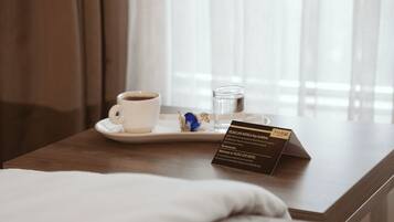 Habitación de hotel con mesita de noche de madera, almohada blanca, una taza de café, un vaso de agua y una tarjeta de bienvenida.