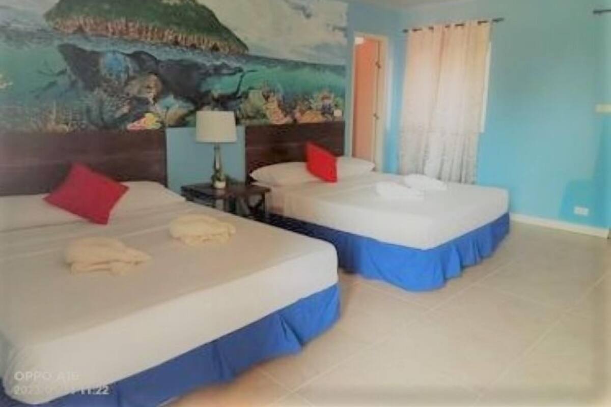 A hotel room with two beds, a mural on the wall, and a window with curtains.