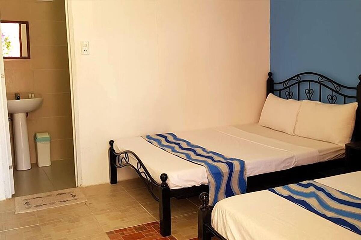A bedroom with two beds, a bedside table with a lamp, a window with a view, and a bathroom with a sink and toilet.