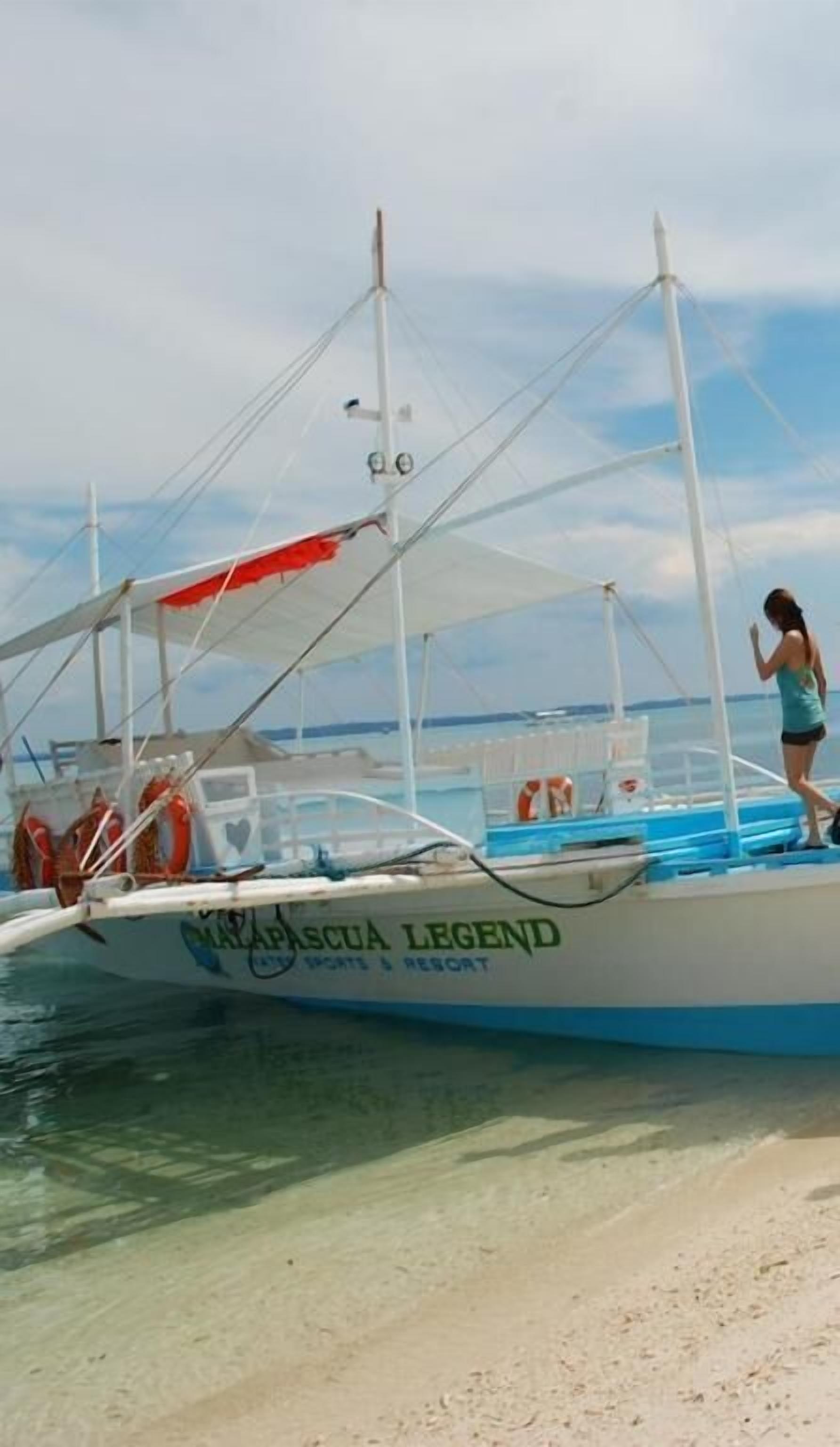 A boat named 'Malapascua Legend' with a clear view of the water and a person standing on the deck.