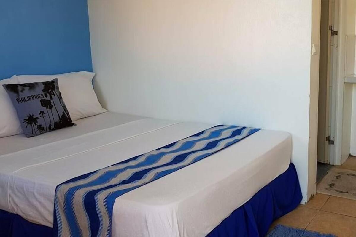 A bed with a white and blue striped bedspread, a pillow with a palm tree design, and a blue wall.