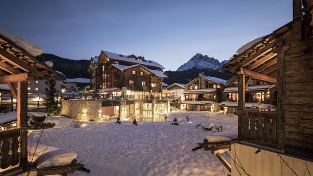 Un village enneigé, avec des bâtiments en bois et une montagne en arrière-plan.