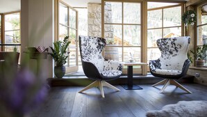 Une pièce avec deux fauteuils à motifs, une petite table et une vue sur un paysage montagneux, visible à travers de grandes fenêtres.
