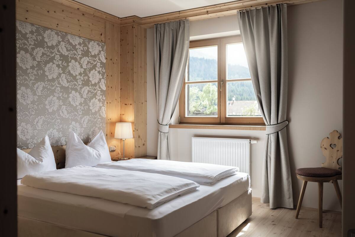 Een slaapkamer met een groot bed, een raam met gordijnen, een radiator en een houten hoofdbord.