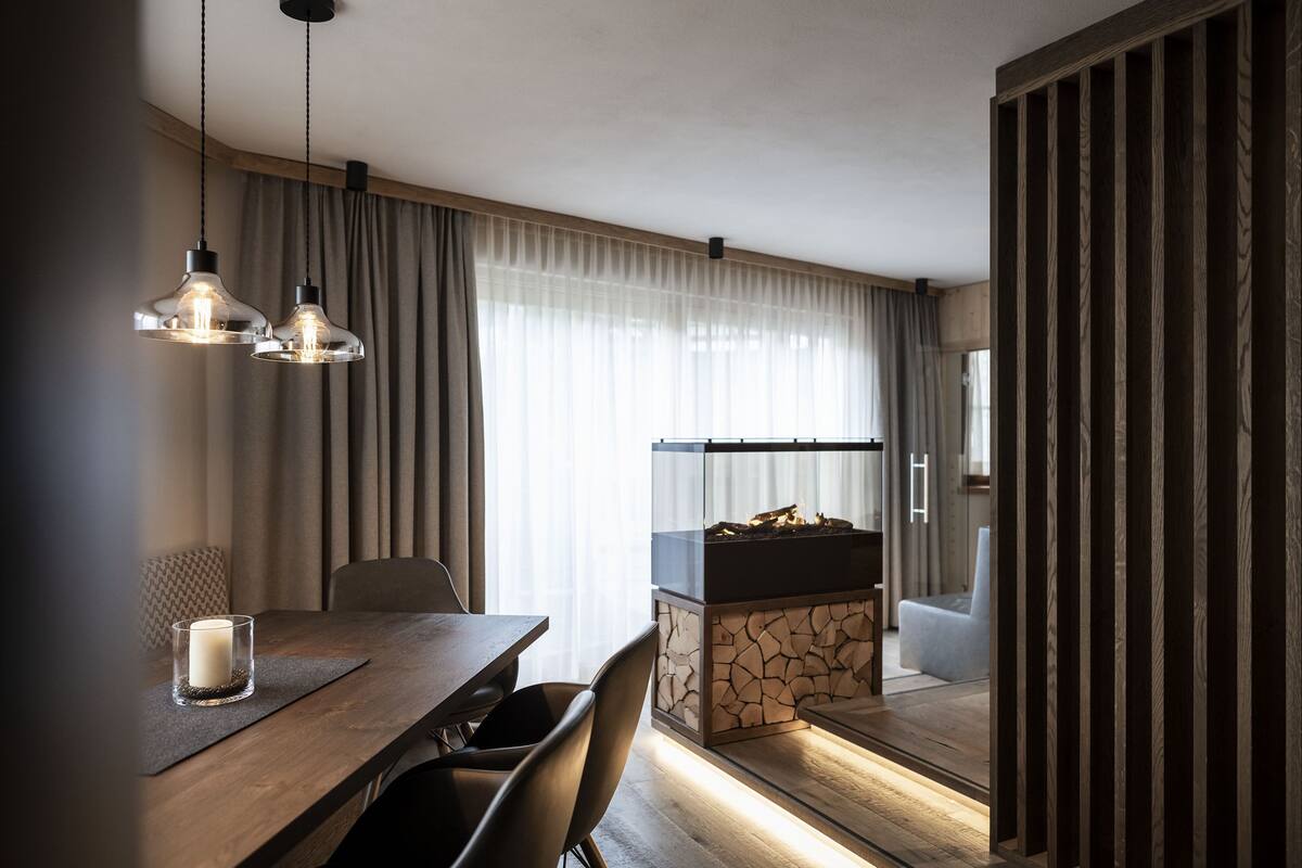 Een moderne eetruimte met een houten tafel, stoelen en hanglampen. Op tafel staat een glazen kandelaar.
