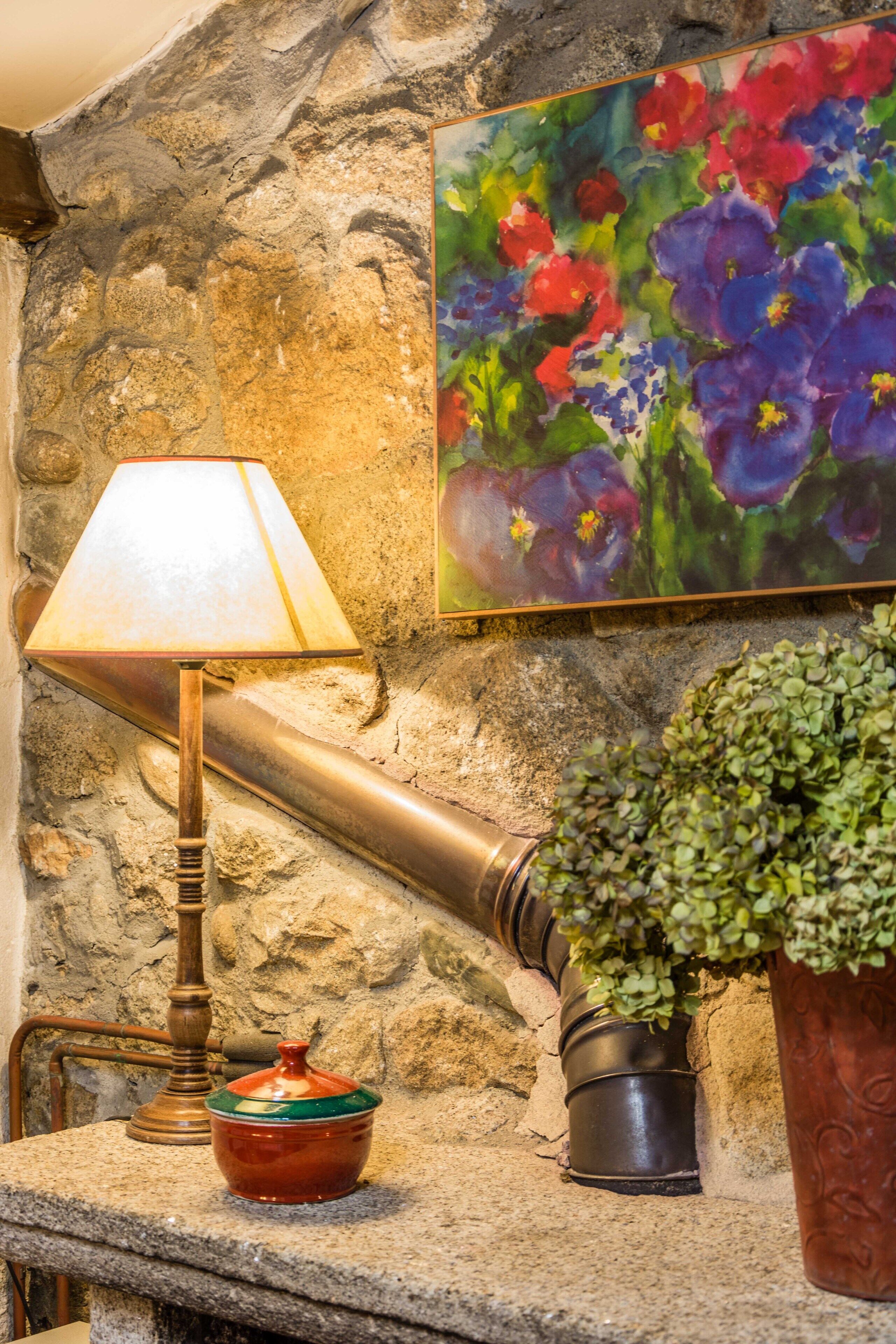 A stone wall with a painting of flowers, a lamp, a small bowl, and a potted plant.