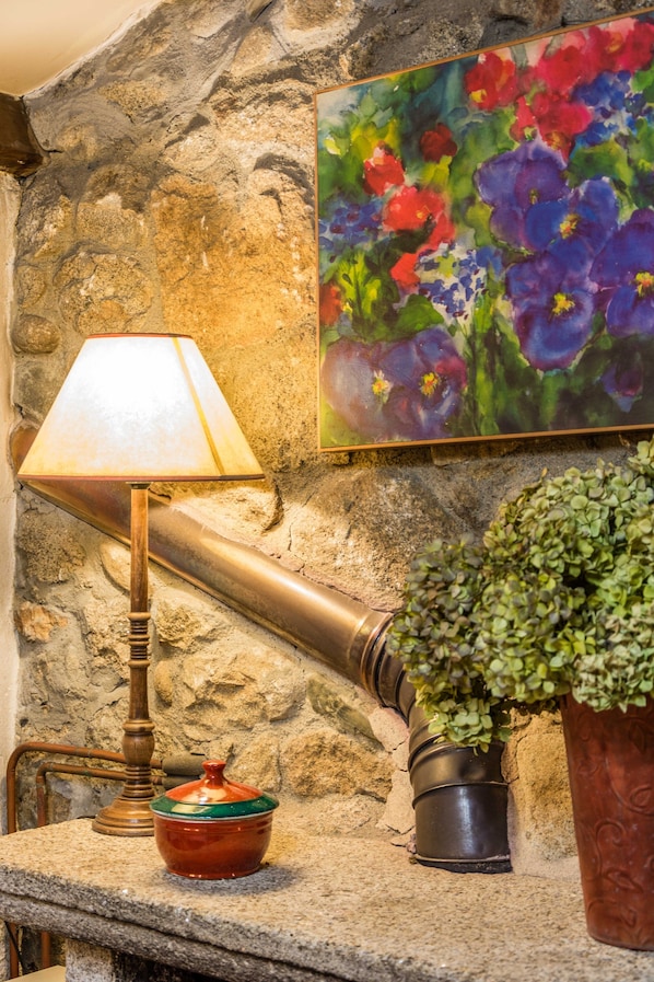 Un mur de pierres sur lequel est peinte une composition florale, une lampe, un petit bol et une plante en pot.